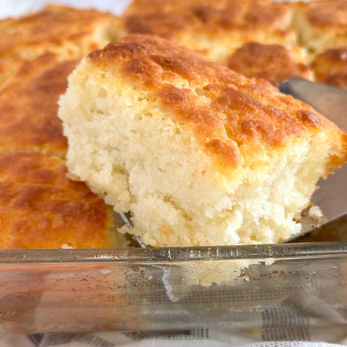 A slice of an Old-Fashioned Buttermilk Butter Swim Biscuit scooped on a spatula from a pan of biscuits.