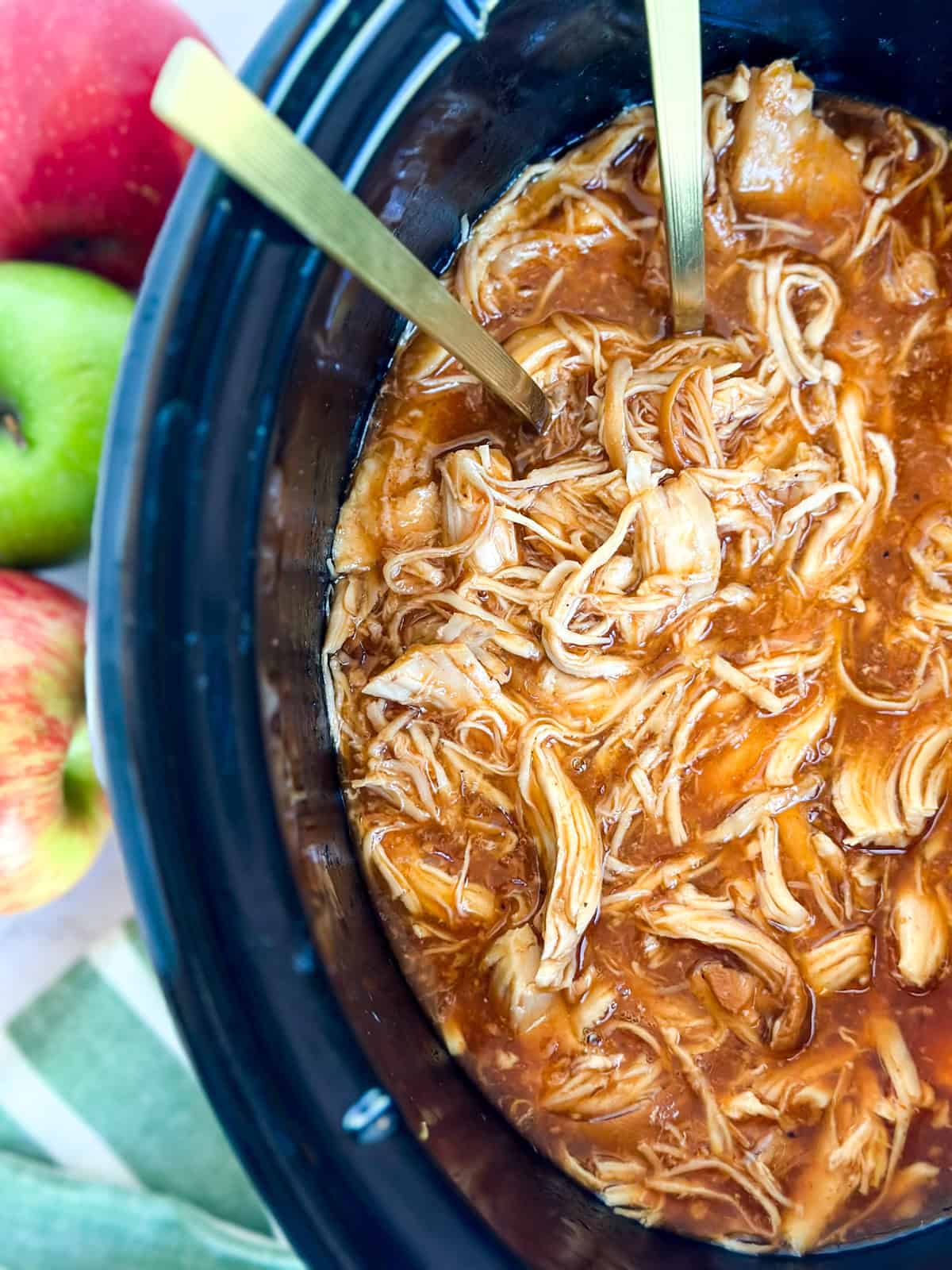 Shredded Apple BBQ Chicken in the Crock Pot with apples around it.