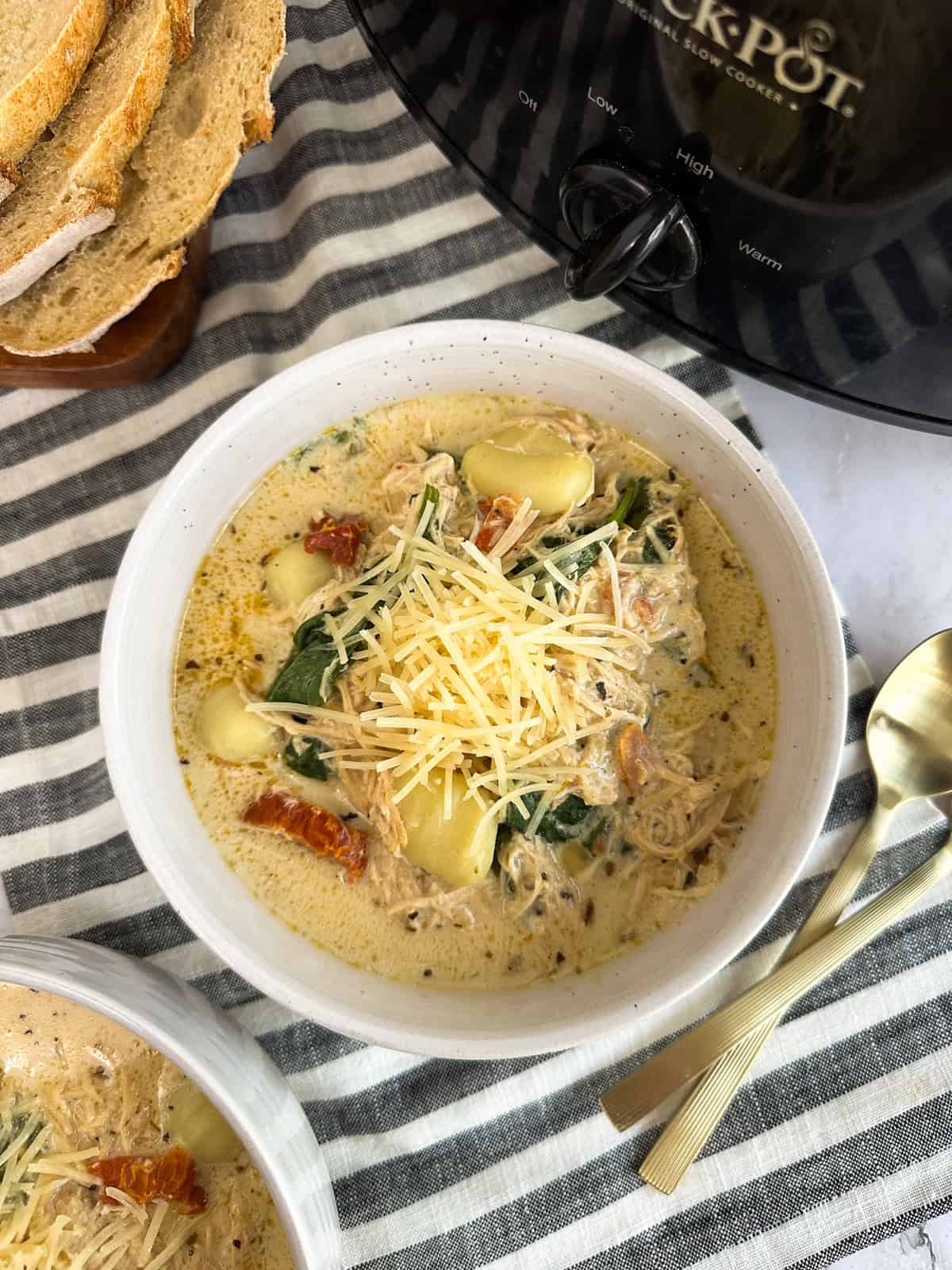 A bowl of Slow Cooker Marry Me Chicken Gnocchi Soup with another bowl and slow cooker next to it.