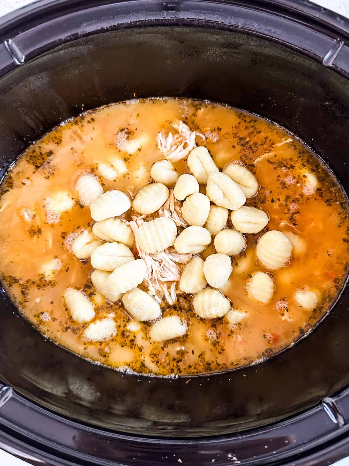 Adding gnocchi to the soup in the slow cooker.