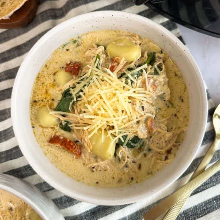 A bowl of Slow Cooker Marry Me Chicken Gnocchi Soup with another bowl and slow cooker next to it.