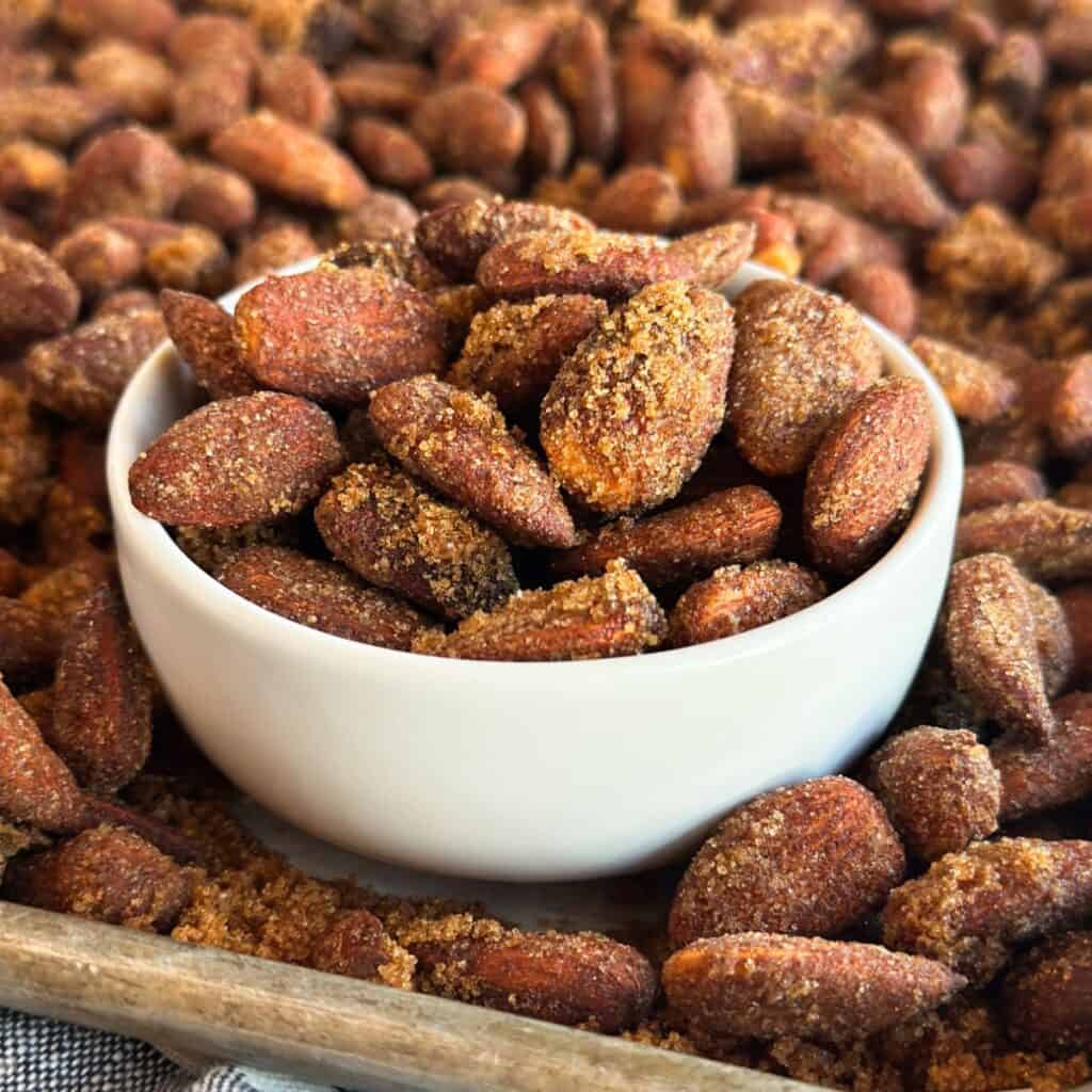 A bowl of Slow Cooker Cinnamon Candied Almonds on a baking sheet filled with almonds.