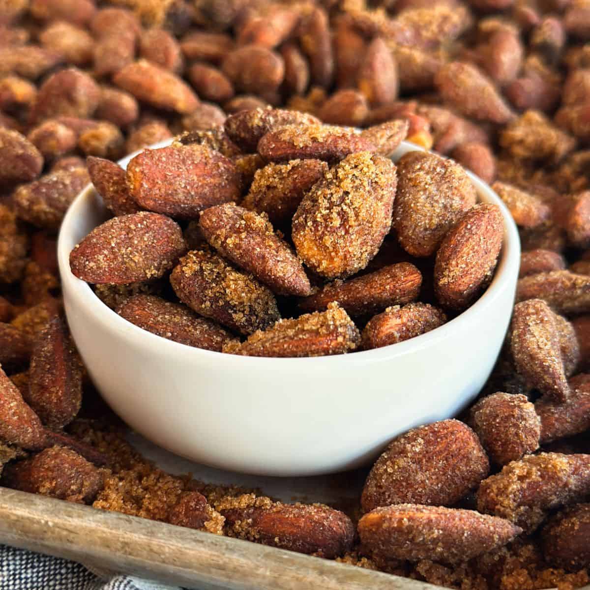 A bowl of Slow Cooker Cinnamon Candied Almonds on a baking sheet filled with almonds.