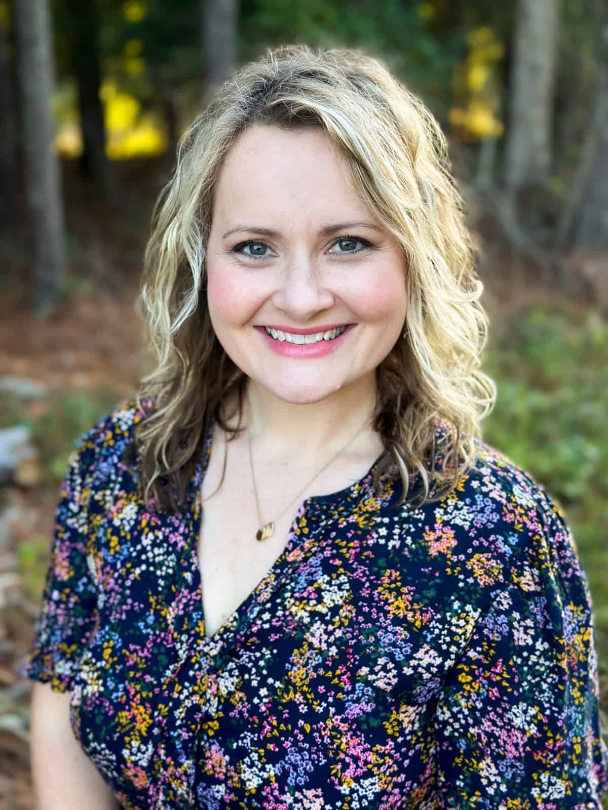 A portrait of a woman smiling at the camera with the woods in the background.