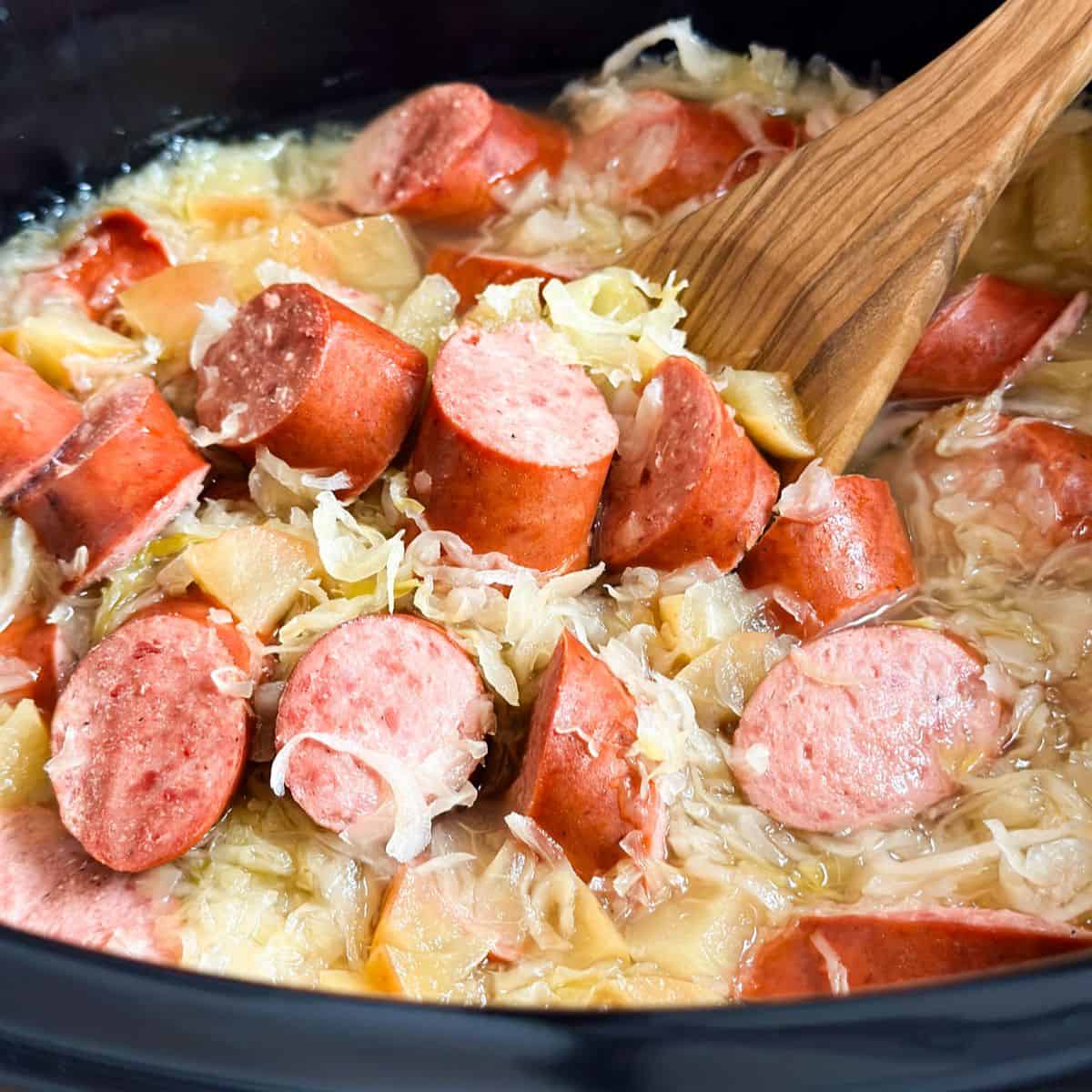 Sausage and sauerkraut in a crock pot with a wooden ladle.